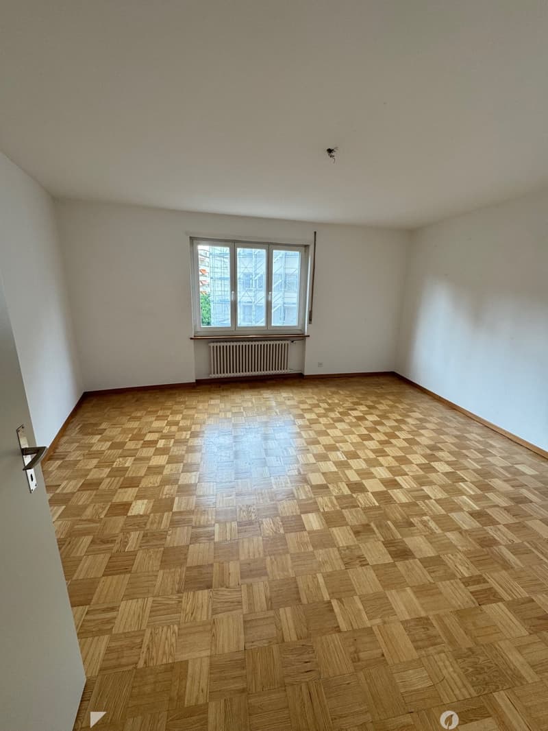 Empty room with white walls, large windows, and a parquet wood floor in a checkered pattern.