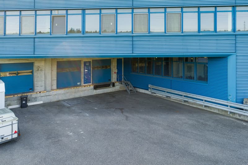A large blue commercial building with multiple windows, a loading dock, and a parking area in front.