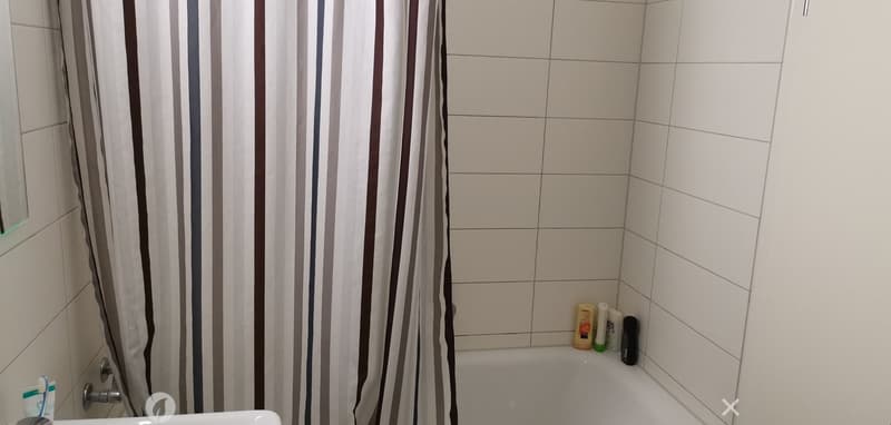 Bathtub, sink, white tiles, shower curtain, bottles on the ledge