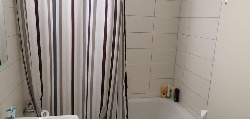 Bathtub, sink, white tiles, shower curtain, bottles on the ledge