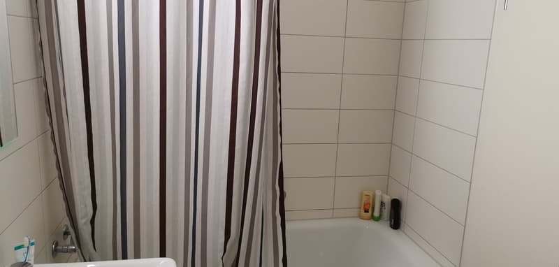 Bathtub, sink, white tiles, shower curtain, bottles on the ledge