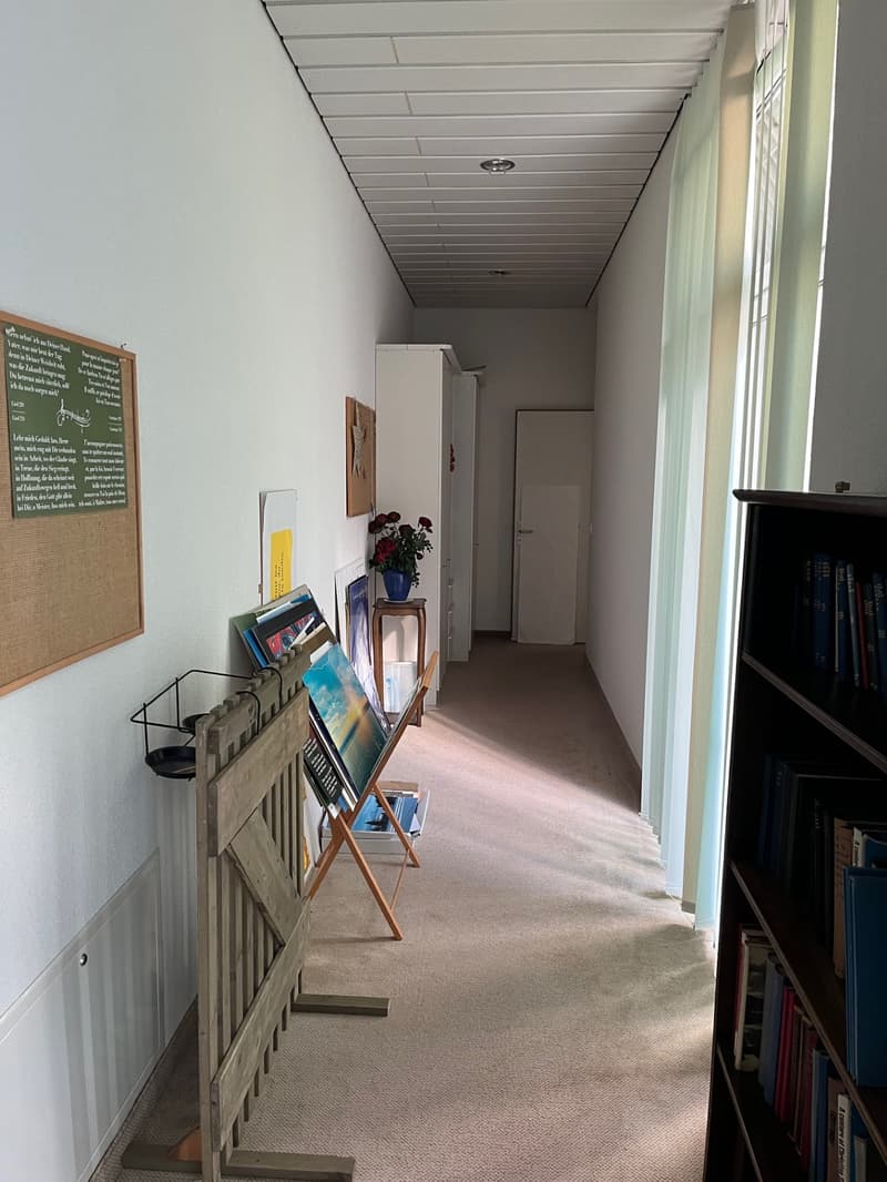 carpeted floor, white walls, bulletin board, picture frames, book displays, door, cabinet