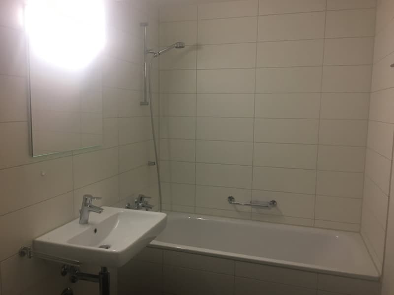 Bathroom with white tiles, bathtub, sink, mirror, shower head and handle