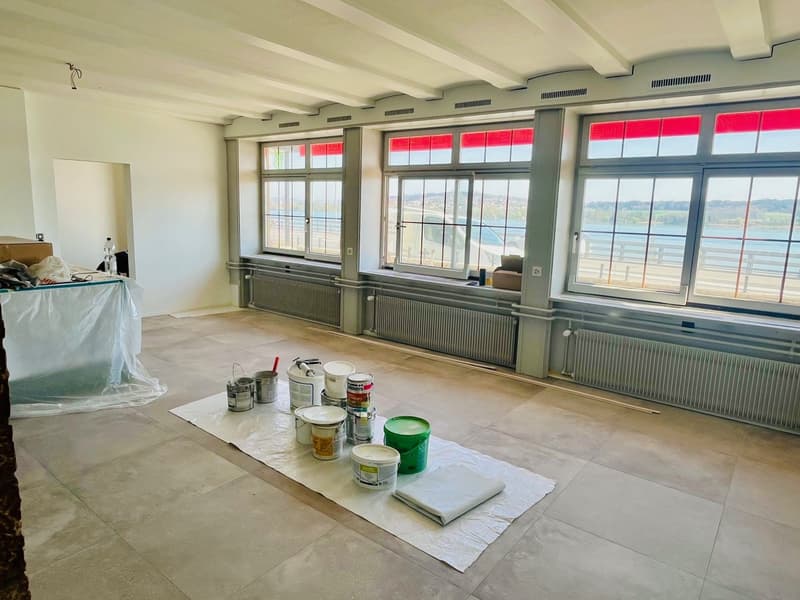 Empty room, large windows, view of the water, covered with white tarp, lots of paint cans on a white cover on the floor