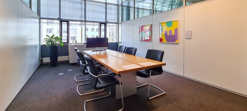 modern conference room, long wooden table, black chairs, monitor, potted plant, glass walls, paintings