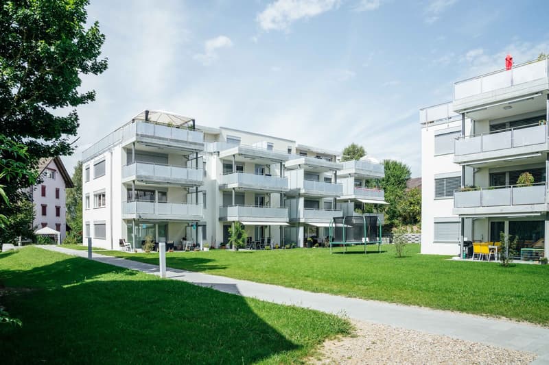 Modern apartment building with multiple balconies, well-maintained green lawn, and a pathway leading to the entrance.