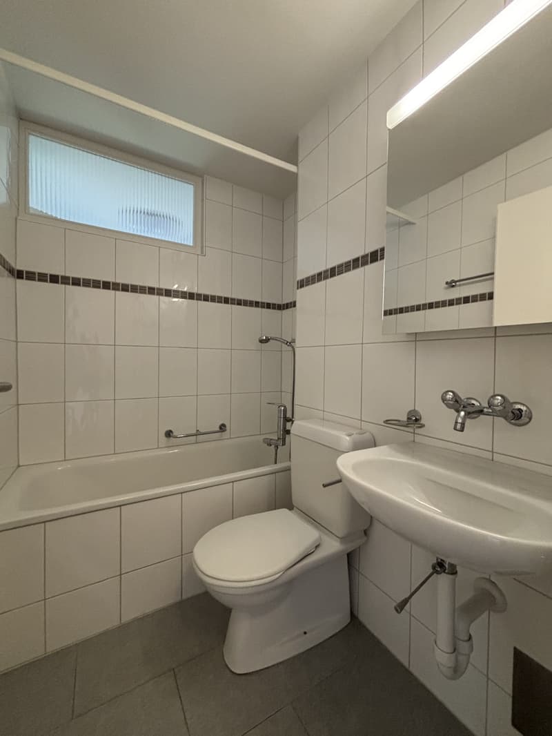 Bathroom with white tiles, bathtub, toilet, sink, mirror, and shower head