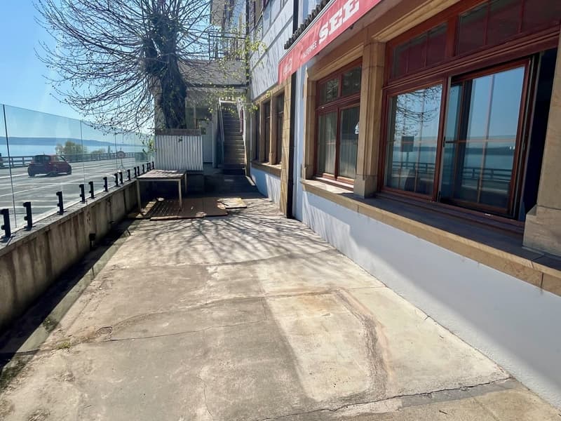 Outdoor area with concrete floor, glass fence, stairs leading to a building, signboard, and a view of the ocean