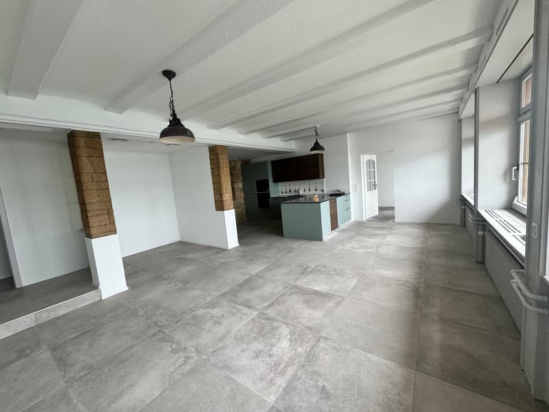 Spacious room, large gray tiles, high ceiling, two lamps, kitchen visible in the background