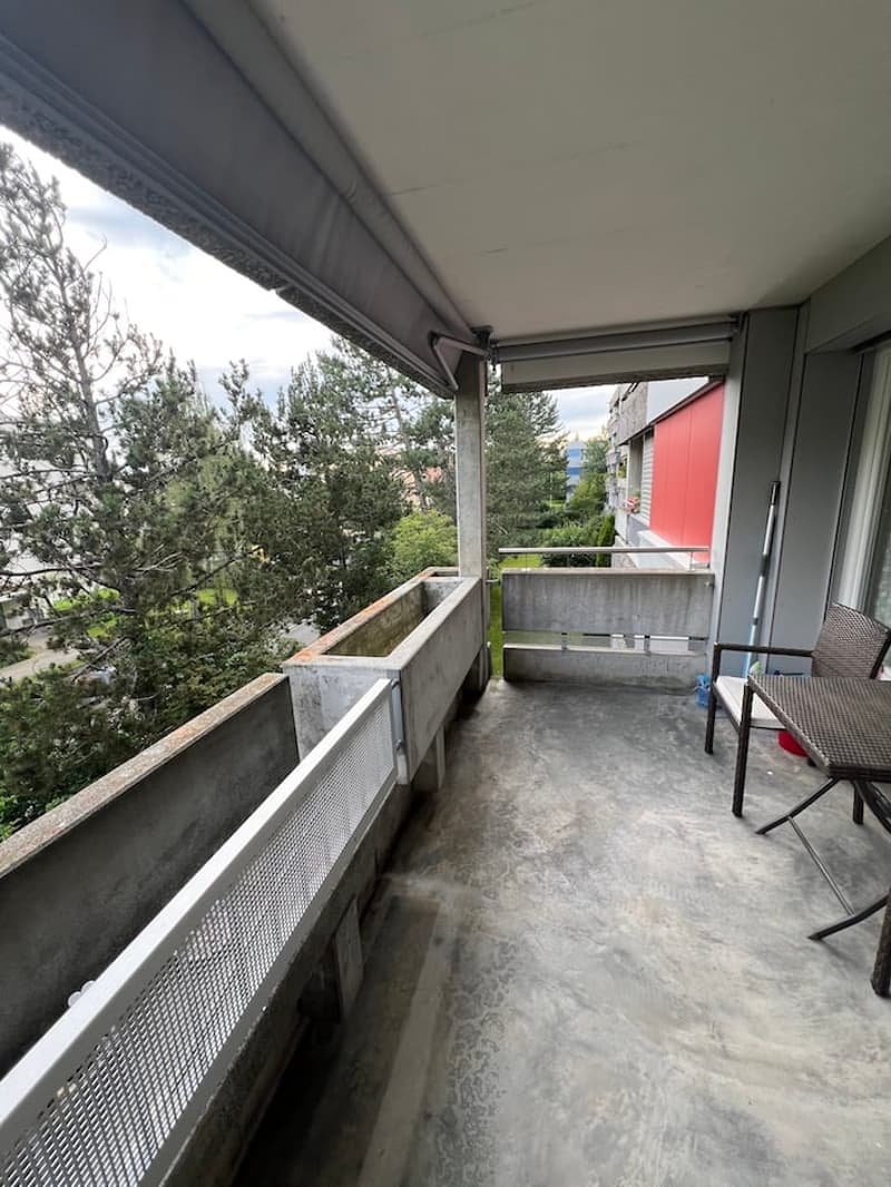 Balcony with concrete railings, metal grates, and a table with a chair