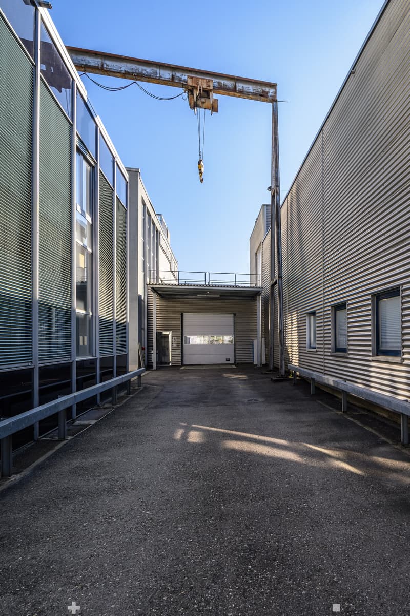 Industrial building with metal walls, large windows, large entrance, large crane over the entrance, empty parking place in front