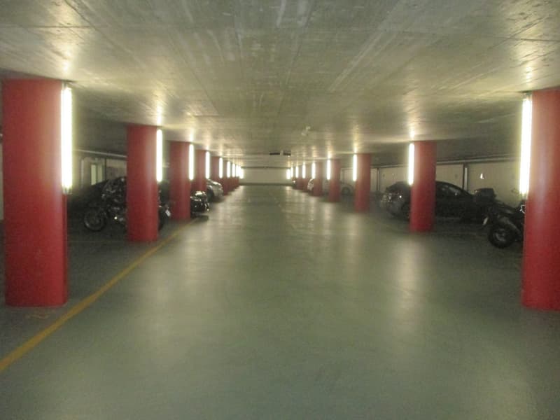 underground parking lot with yellow lines marking parking places, vertical red pillars, fluorescent ceiling lights