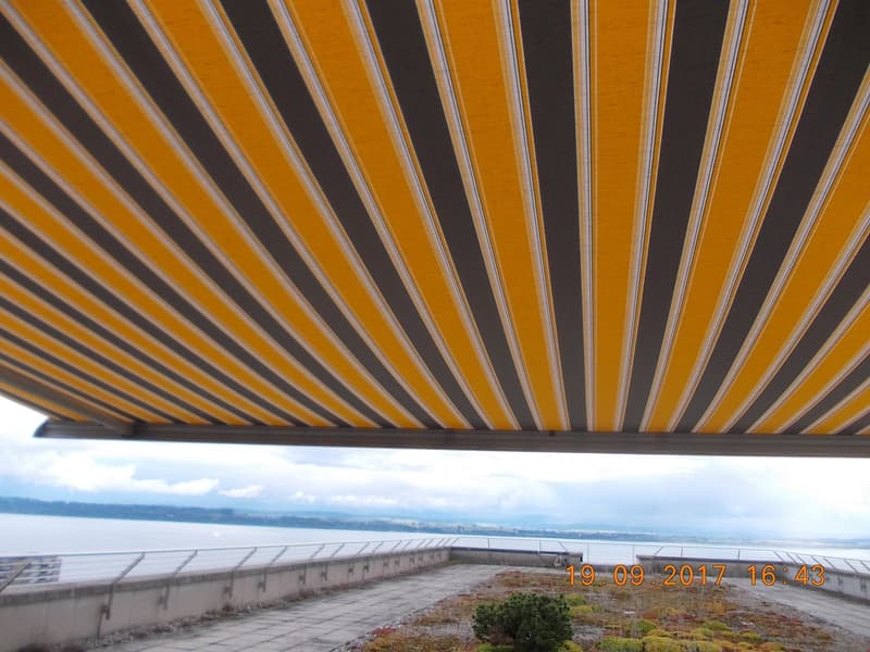 A photo of a yellow and gray striped awning over a rooftop terrace with a view of the ocean