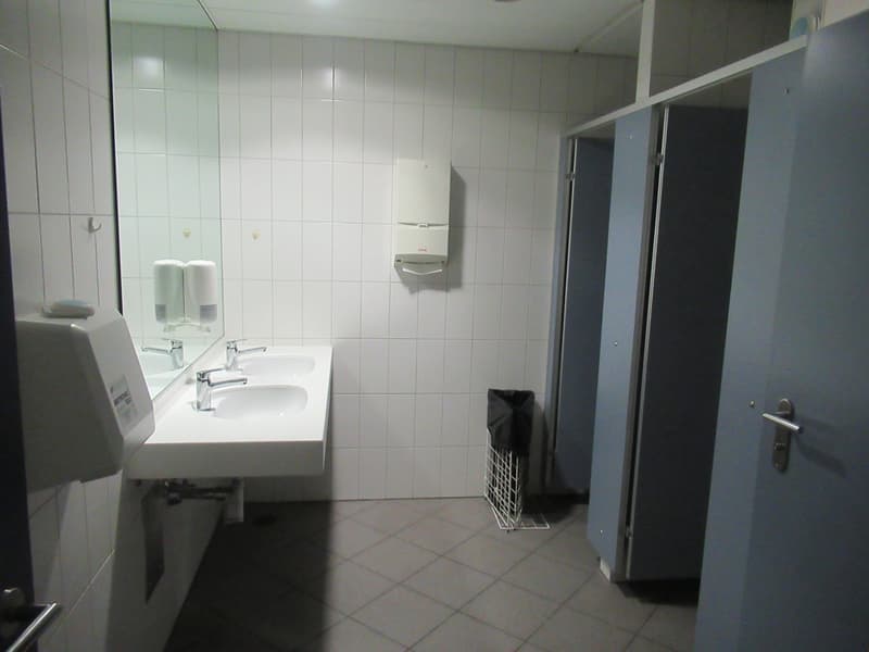 A bathroom with two sinks, a mirror, and two toilet stalls with trash cans. There are no visible features in the list