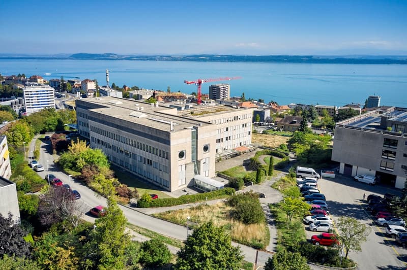 Two-story building with large windows and parking lot overlooking a lake and city.