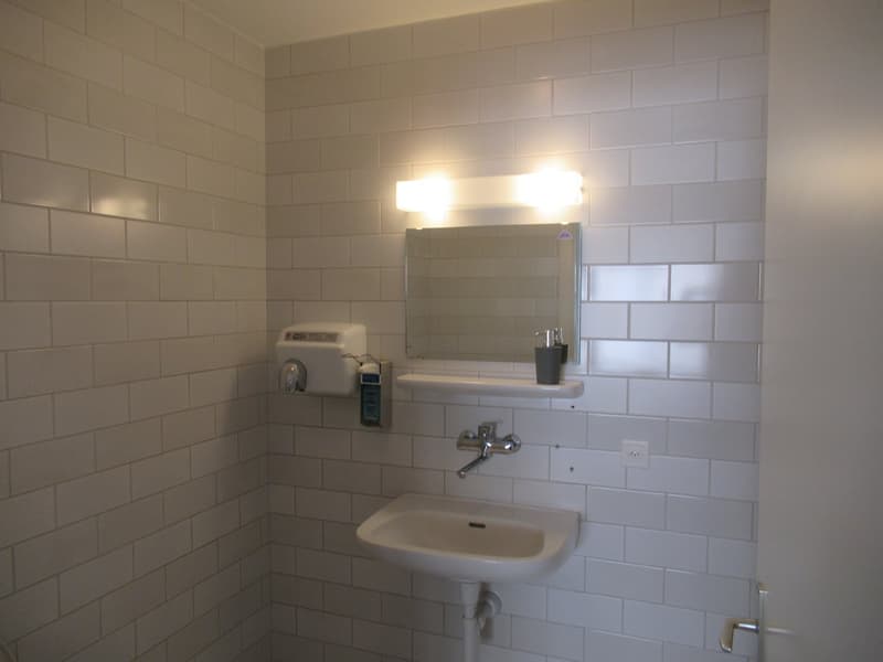 Bathroom with tiled walls, mirror, sink, faucet, towel dryer, power outlet.