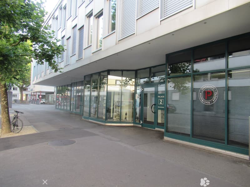 Modern building with glass facade, entrance with logo and number, glass doors, bicycle parked