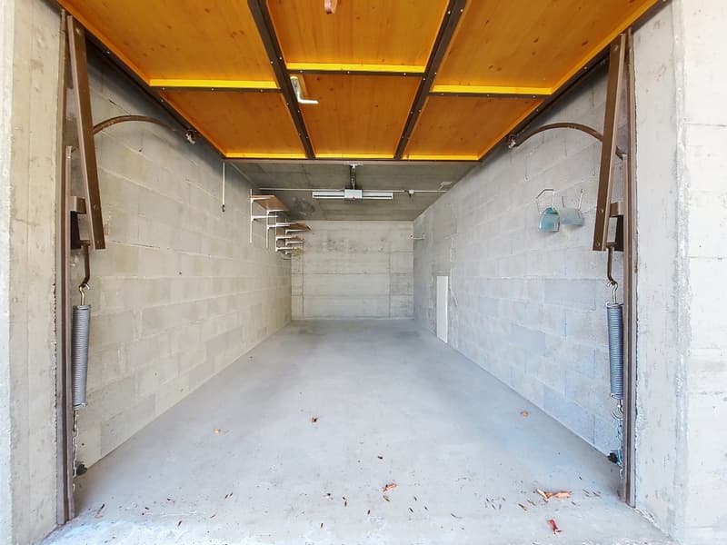 Empty concrete garage with wooden ceiling, metal shelves, and spiral springs on the doors
