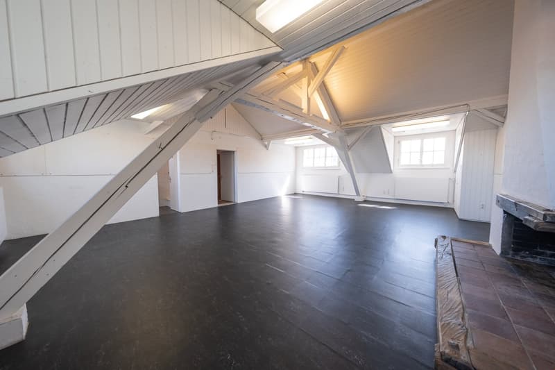 Attic room, exposed wooden beams, high ceilings, black wooden flooring, white walls, windows, fireplace
