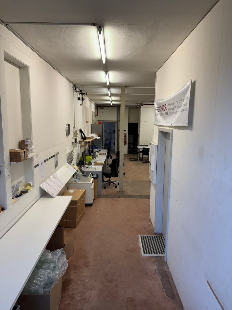 empty room with office desks, cabinets, boxes, shelves, fluorescent lights, and a banner on the wall