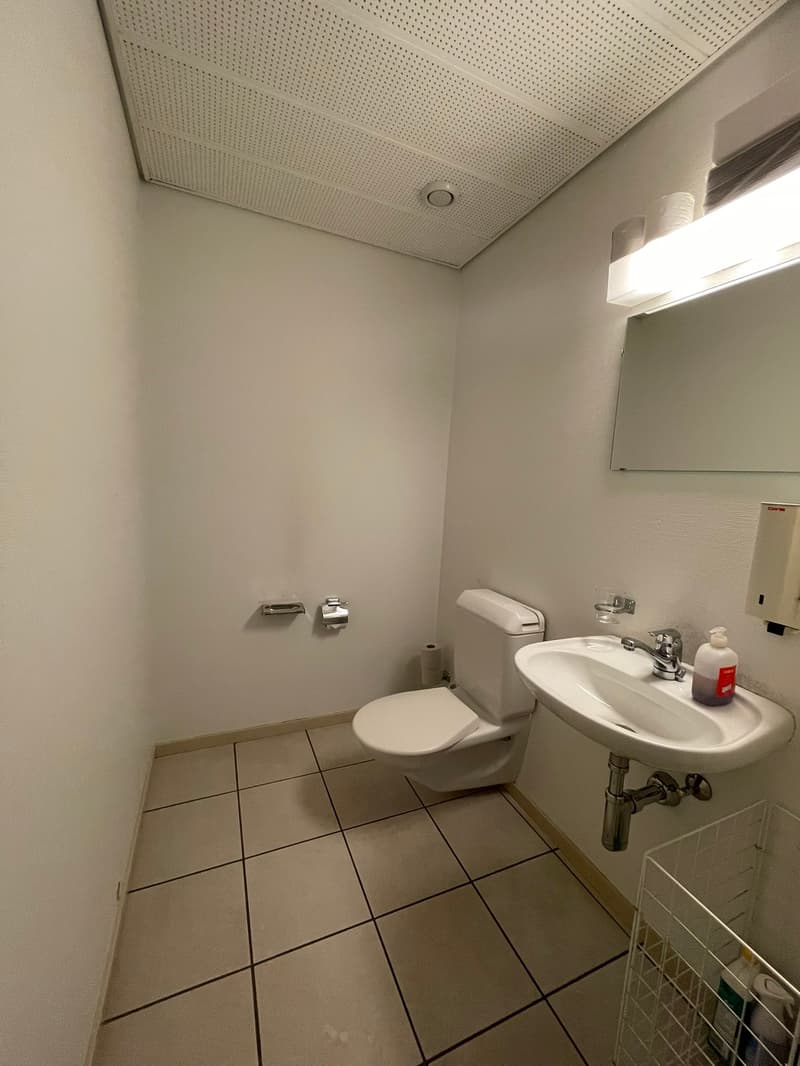 small bathroom with white walls, tiled floor, white sink, white toilet, mirror, and a soap dispenser