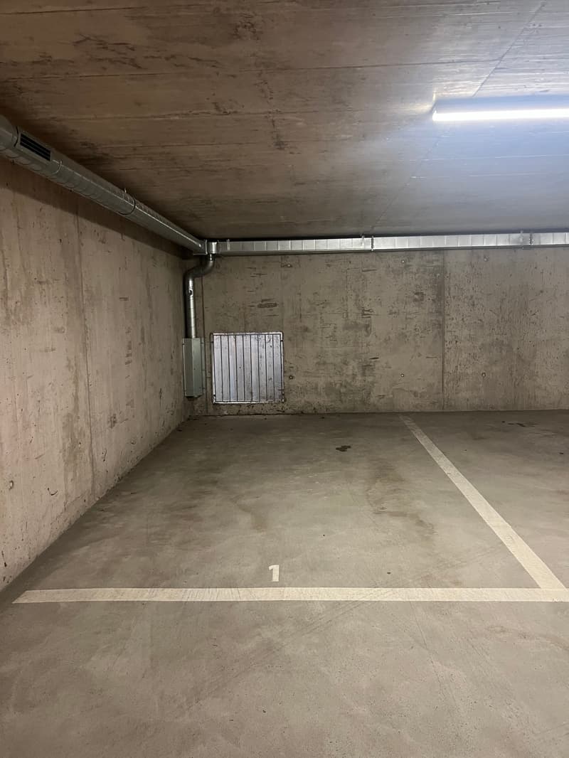 An empty parking lot with concrete walls, a small ventilation grill, and a number '1' on the floor.