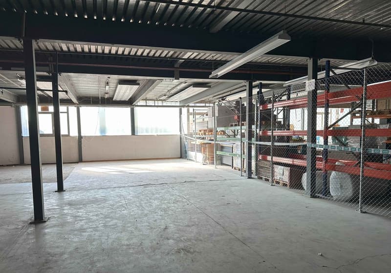 Large open space with concrete floor, metal shelving units, and overhead lighting. The space appears to be a warehouse or storage facility.