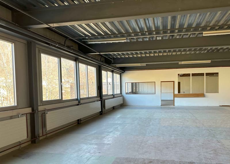 Large open commercial space with high ceilings, exposed metal beams, and large windows overlooking the outdoors. The space appears to be unfinished, with a concrete floor and minimal interior features.