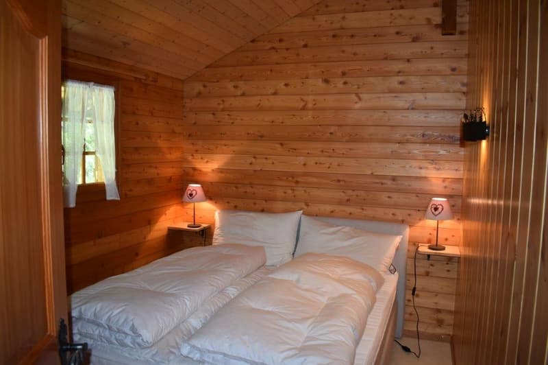 Cozy wooden cabin bedroom with a double bed, bedside tables with lamps, and a fireplace visible in the room.