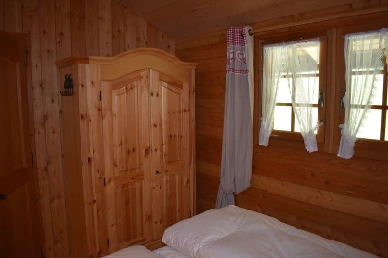Wooden cabin-style bedroom with a wooden armoire, curtains, and a bed with a white comforter