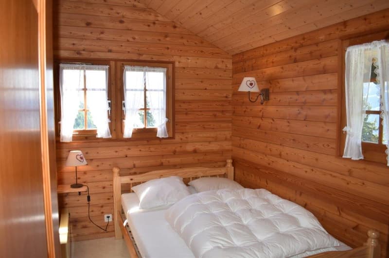 Cozy wooden cabin bedroom with a large bed, wooden walls and ceiling, and a small fireplace on the wall.