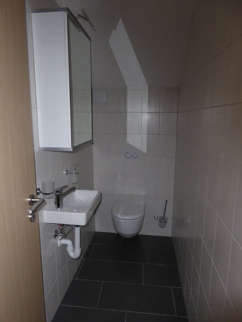 Small bathroom with a white sink, a white toilet, and a white cabinet with a mirror. The floor and walls are made of white tiles. There is a soap dispenser and a glass cup on the wall next to the sink.