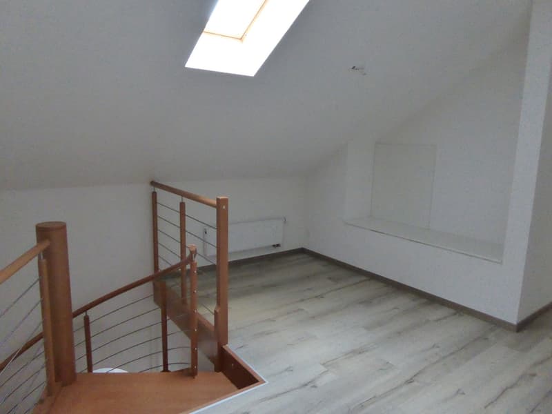 Empty room with wooden staircase, floor with laminate, white walls, skylight, and a bench along the wall