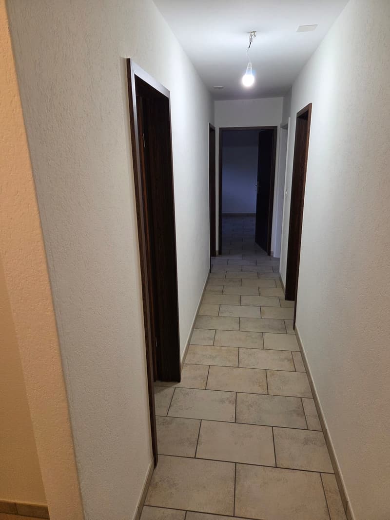 long hallway, white walls, brown tile floor, closed doors