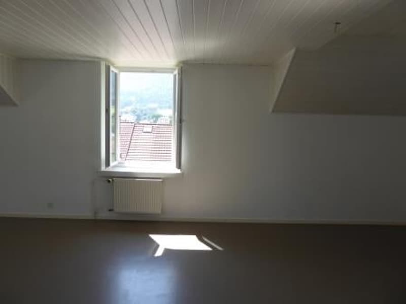 Bright room with white walls, wooden ceiling, and a large window providing natural light. The room appears to be a bedroom or living space.