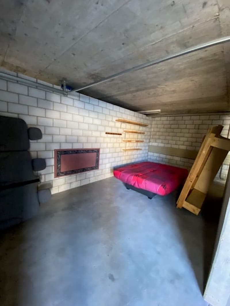 small room with a bed, tiled wall, shelves, and an object on the floor
