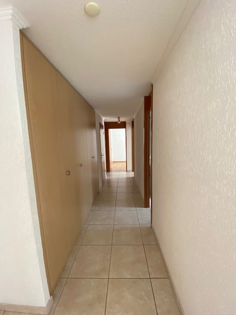 tiled floor, white walls, wooden doors, a door at the end of the hallway, lamps