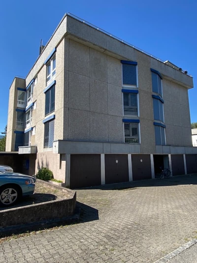 2 story apartment building, gray concrete, blue shutters, garage, parking area