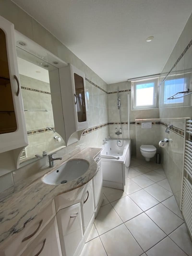 Modern bathroom with bathtub, toilet, sink, mirror, and radiator