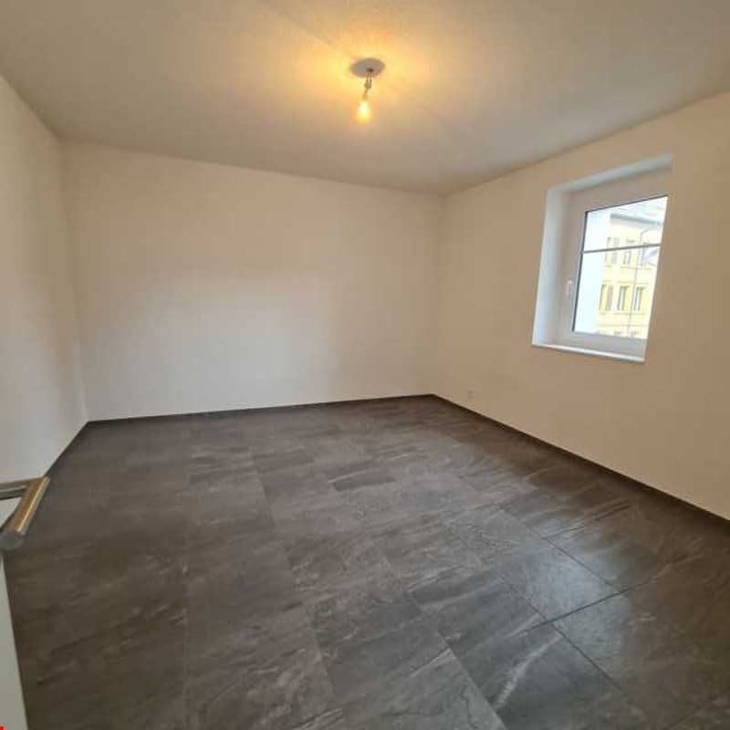 Empty room with gray tiles, white walls, window overlooking building, ceiling light