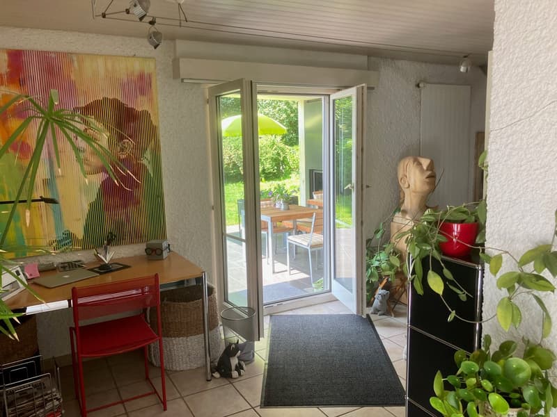 desk, chair, plants, art painting, sliding door with glass panels, rug, office lamp, statue, trash bin, cabinet, laptop, pen, pencil, wastepaper basket, outdoor seating with table and chairs, green umbrella, grass field, trees