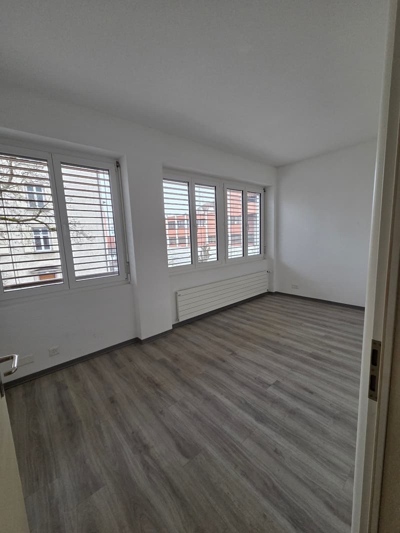 empty room with wooden floor, white walls, large windows, heater