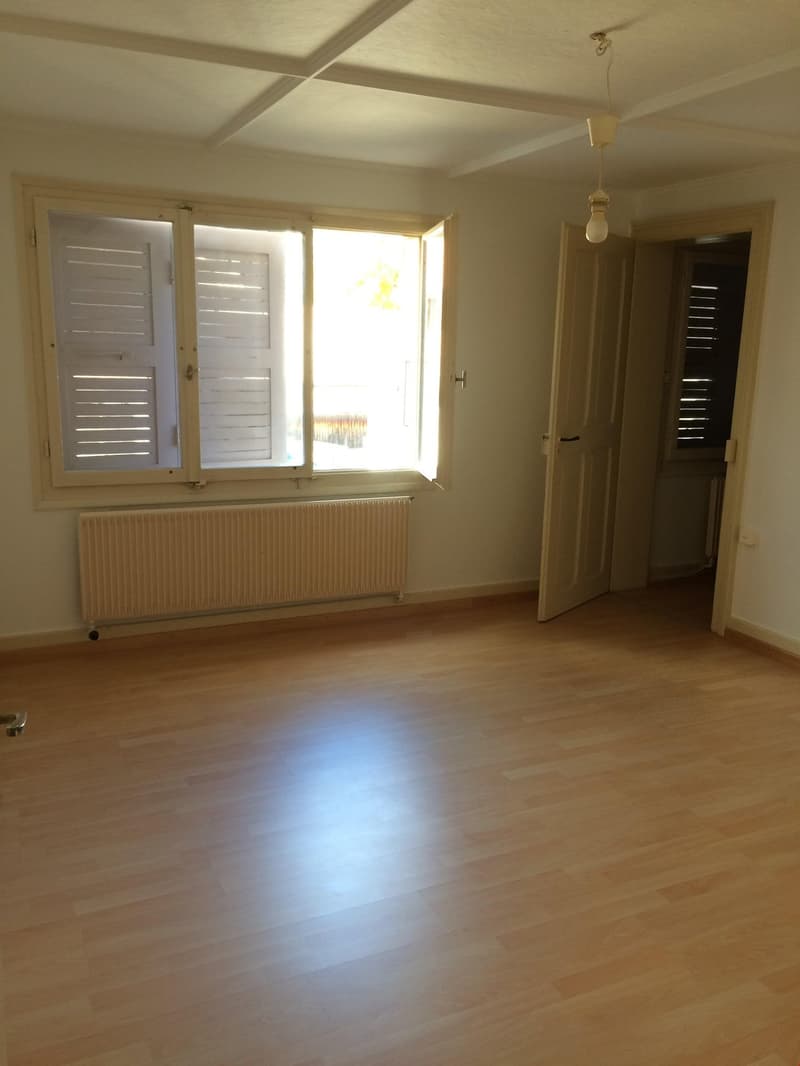 empty room, wooden floors, white walls, large windows with shutters, a radiator is mounted on the wall under the windows