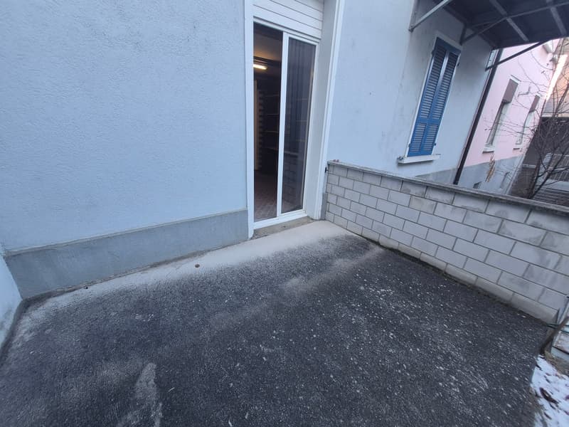 Empty balcony with concrete floor, closed sliding door, white brick walls, open area to the right.