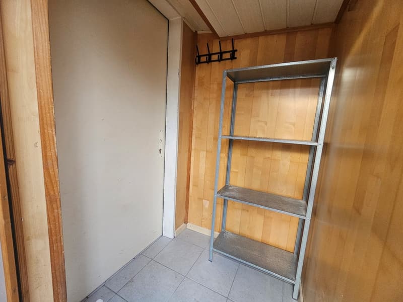 Empty room with wooden wall, tiled floor, white door, metal shelf