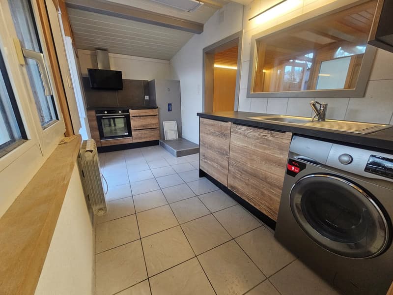 tiled kitchen, large window, electric stove, oven, washing machine, sink with faucet, wooden cabinets