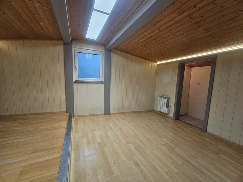 Empty room with wooden floor, wooden wall panels, a window, a radiator, and ceiling lighting