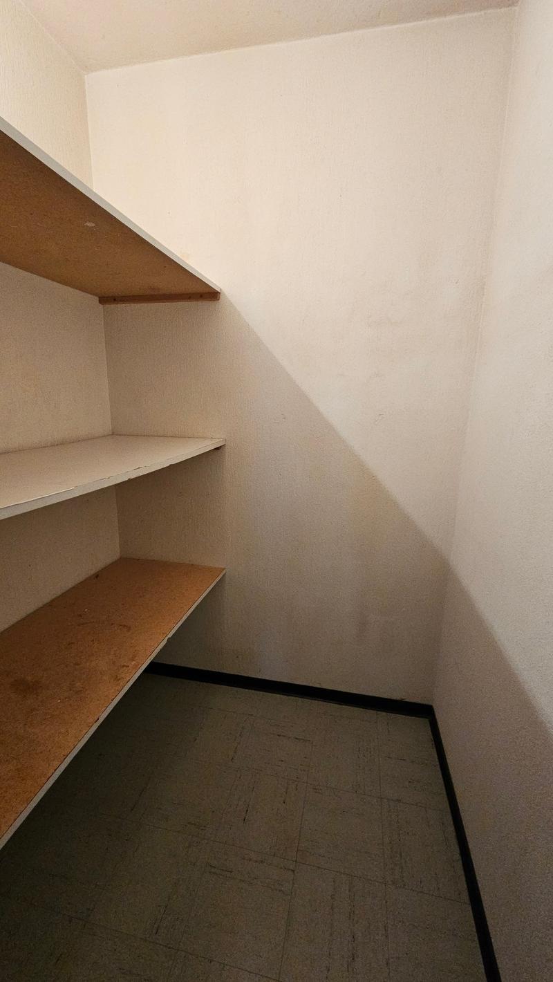Empty room with white wall and wooden shelf. Tiled floor.
