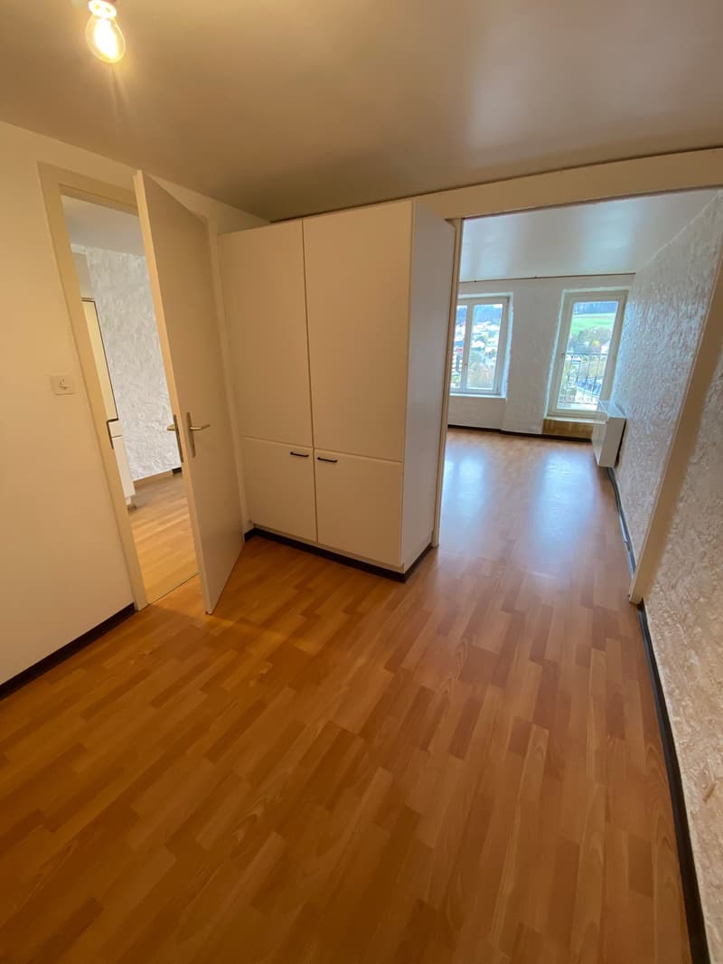 Empty room with wooden floor, white walls, large windows, and a white wardrobe.