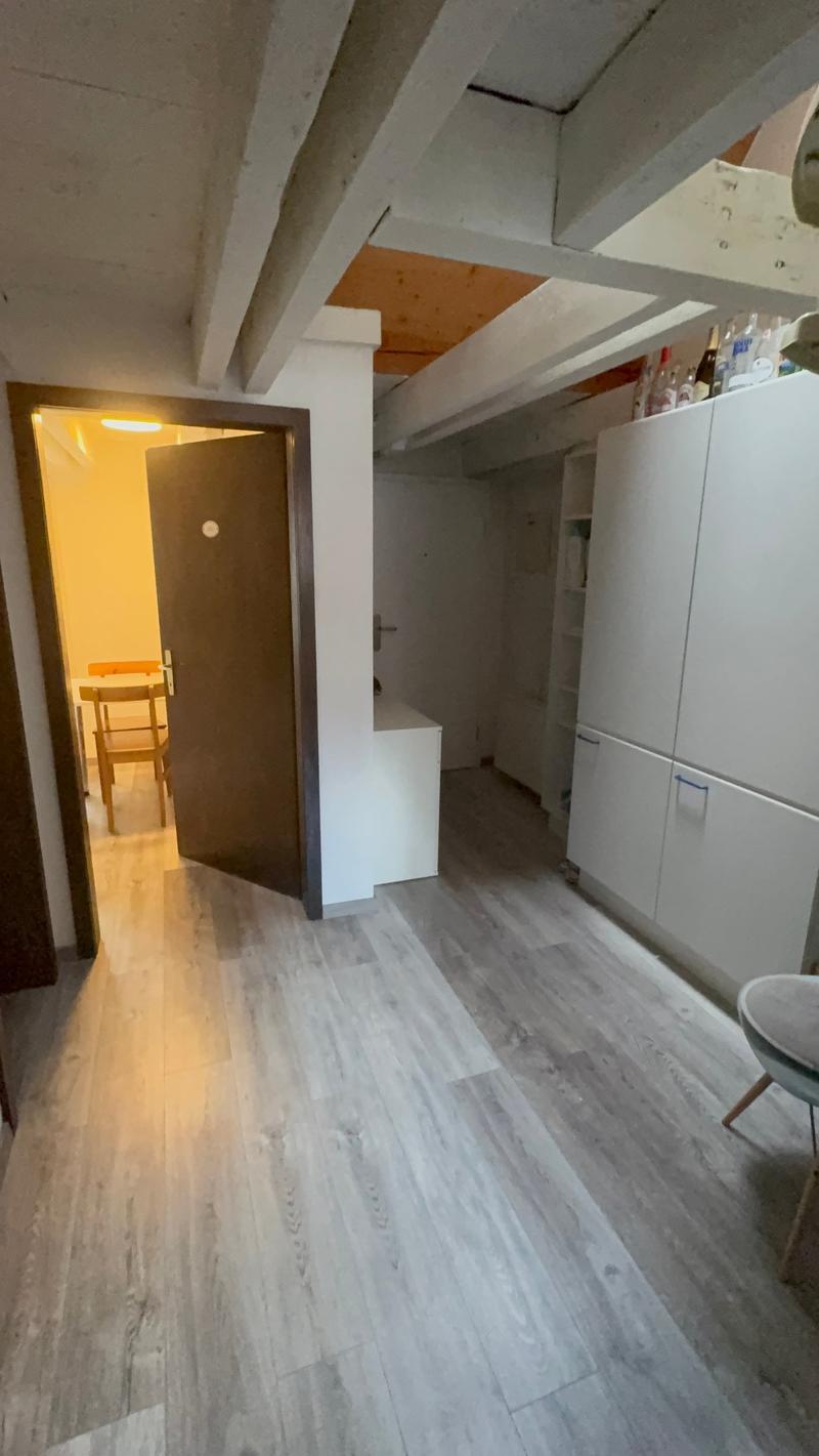 Empty room with wooden floor, white walls, open door, small table and chairs in the background, white cabinets on the right side